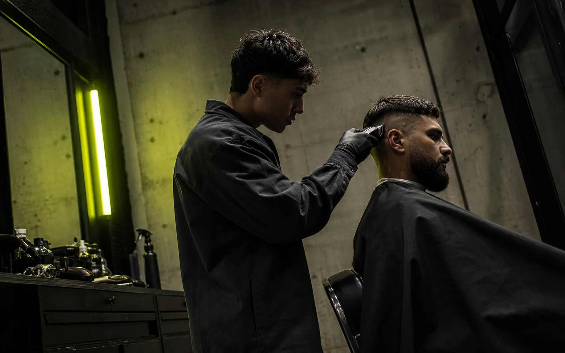 Barber finishing a skin fade under an acid-green striplight