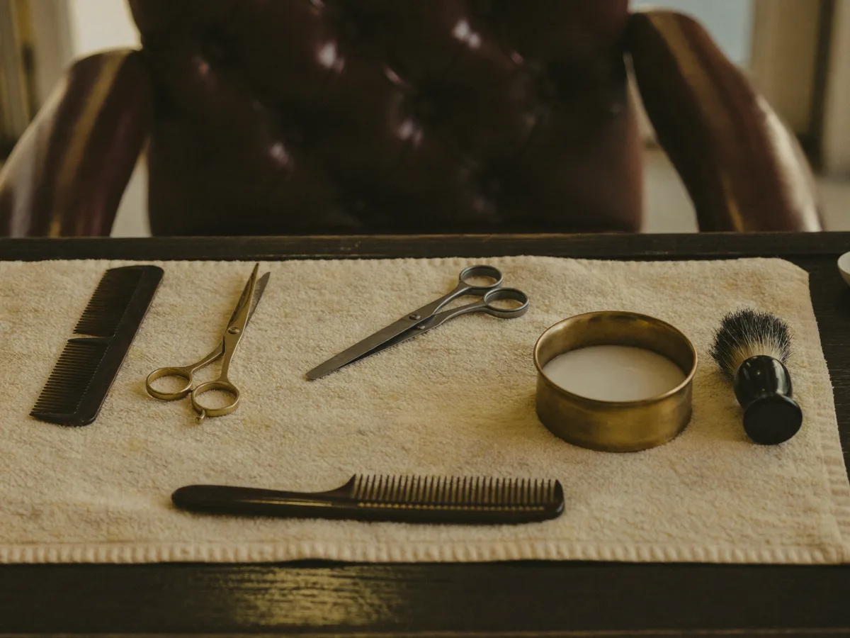 Scissors, combs and shaving soap laid out on a linen towel by an oxblood chair