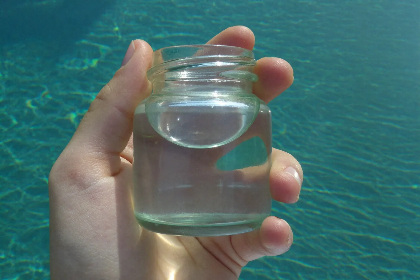 Water sample jar held against the light beside a pool