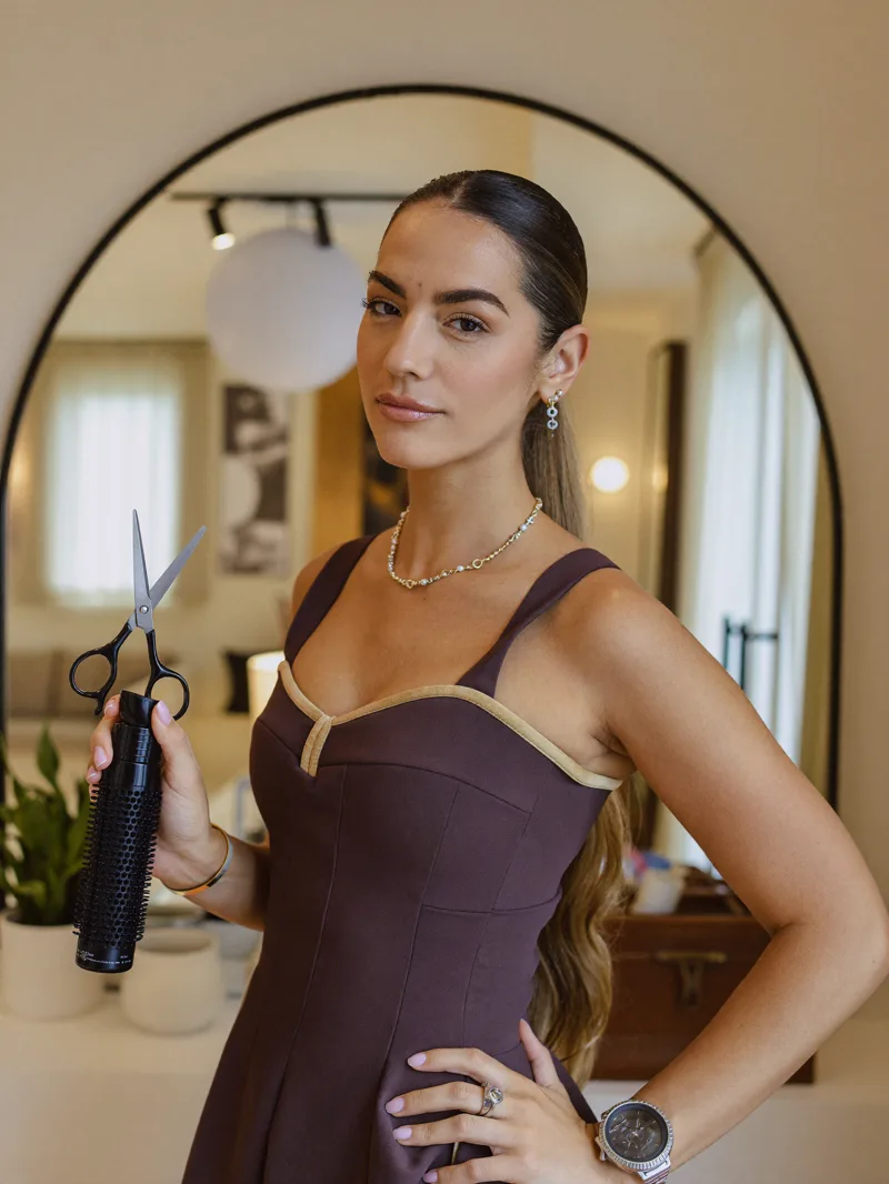 Stylist with scissors and round brush in front of an arched mirror